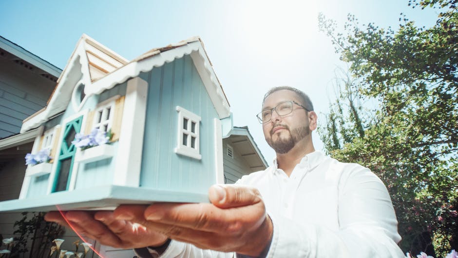 A man holds a miniature house model outdoors on a sunny day, symbolizing home buying