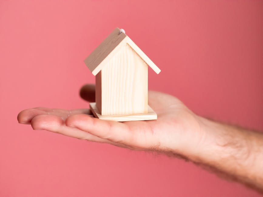 Wooden house model in hand symbolizing real estate concepts on pink background