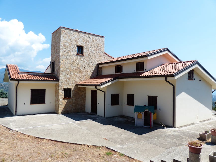 Spacious family house featuring a stone facade and red tile roof, set outdoors under a bright blue sky