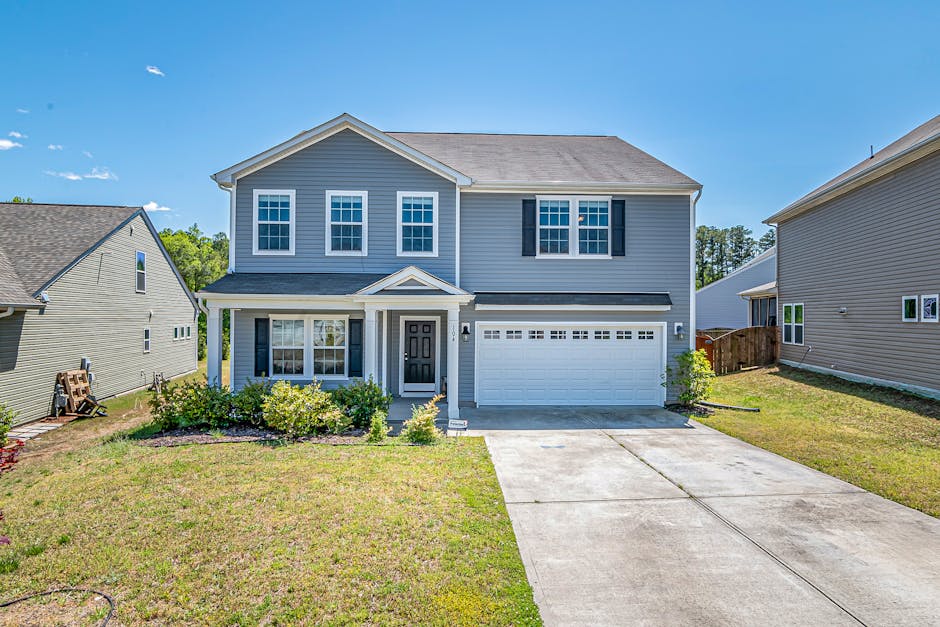 A modern two-story house with a large driveway and landscaped front yard under clear blue skies.